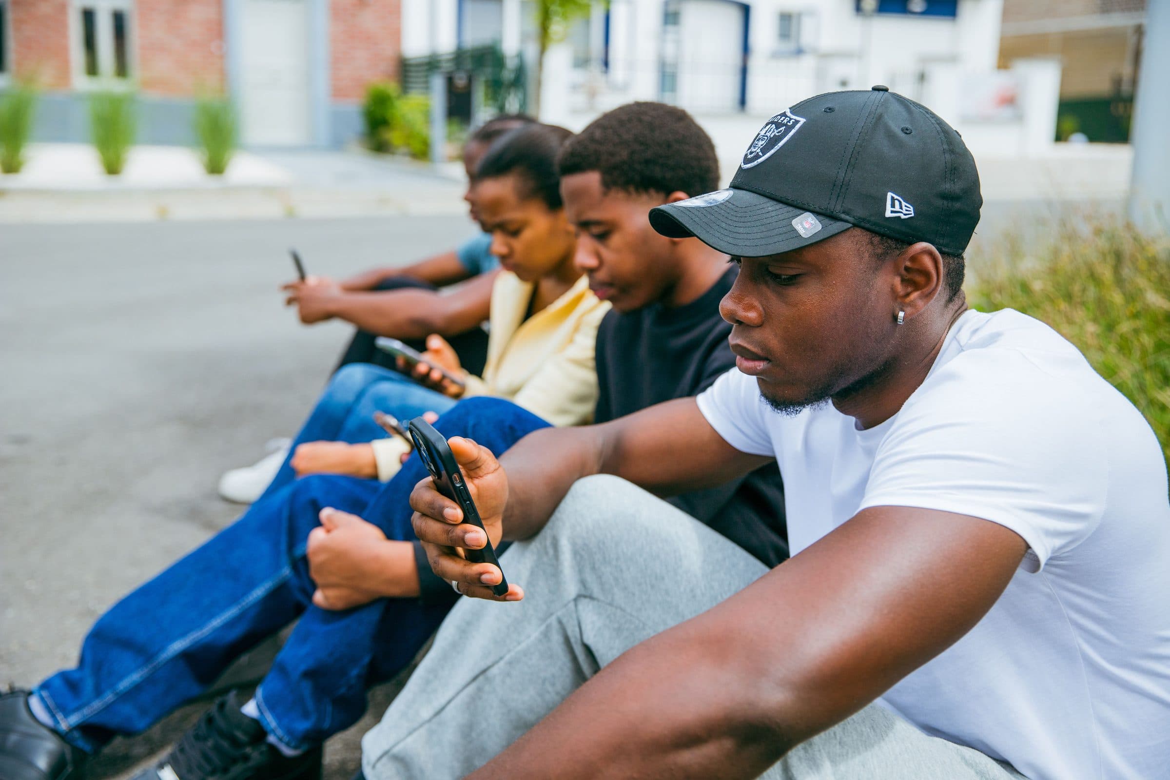 Trois jeunes assis en bord de trottoir, chacun concentré sur son téléphone.